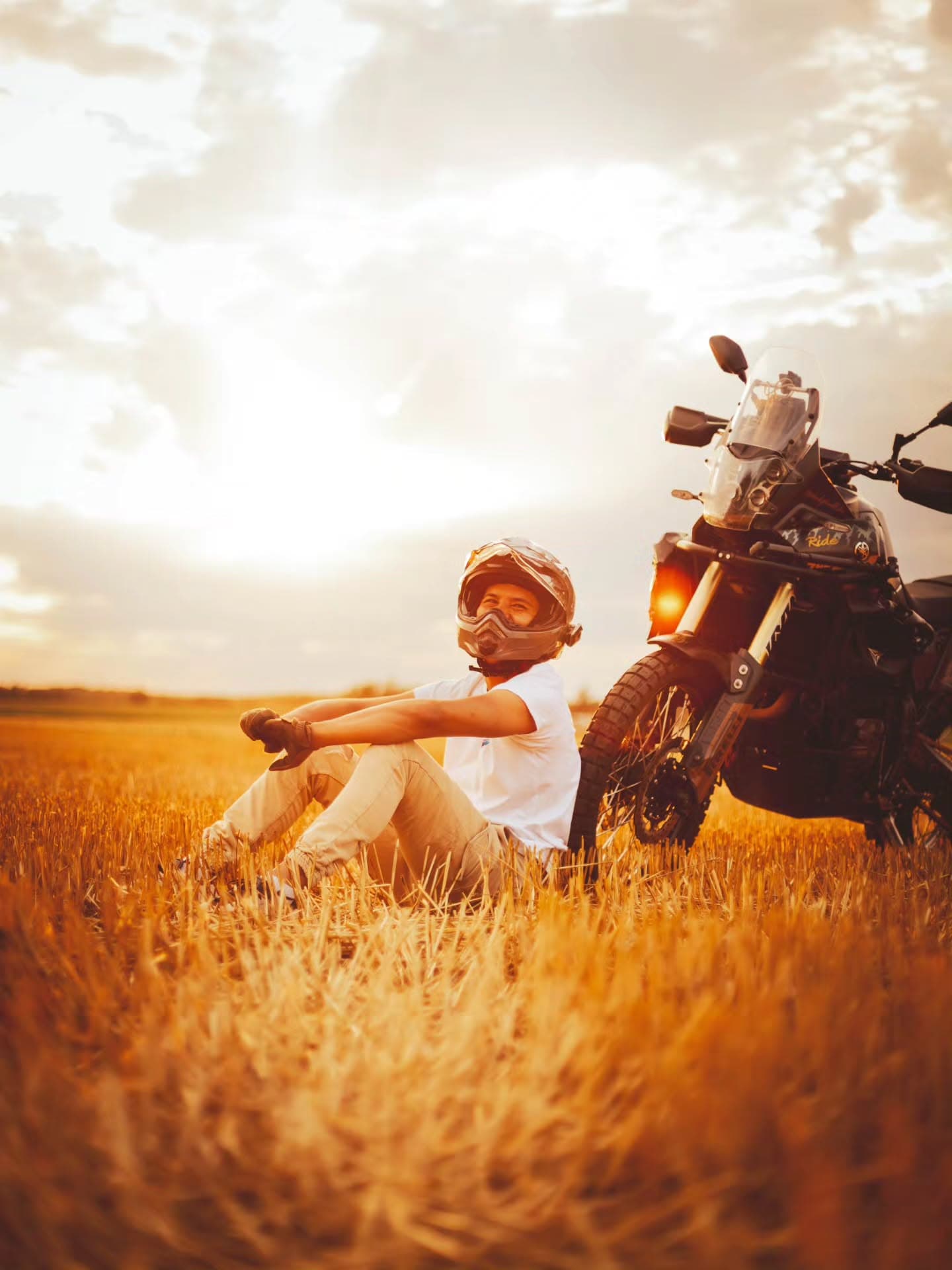 Photographie lifestyle de produits dans un champ avec un motard acoudé à sa moto et soleil couchant